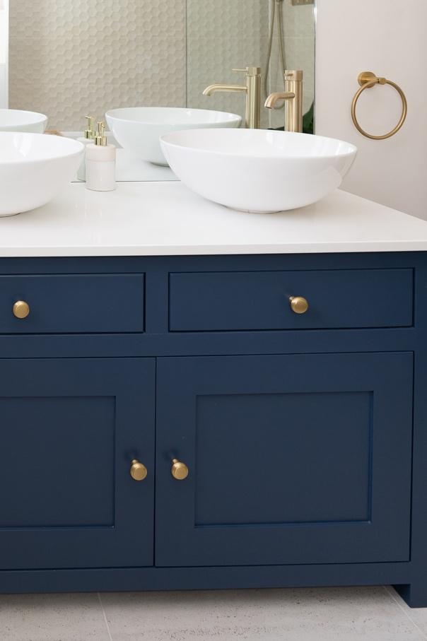 Closeup of a Navy-Blue Bathroom Vanity with a White Counter, Matching Sink Bowls, and Gold Fixtures