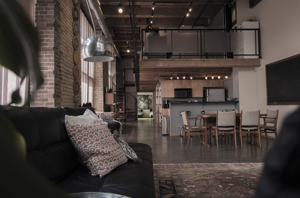 A Two-Story Studio Apartment Featuring Exposed Brick and Beams, Accent Lighting, Custom Kitchen Cabinets, and Cozy Furniture