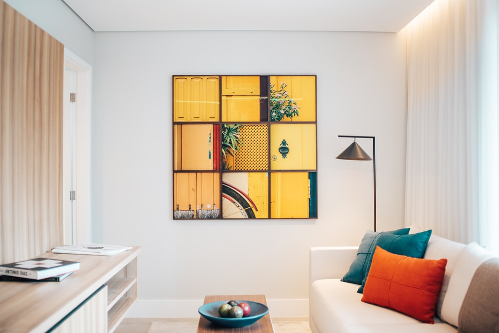  A Living Room with a Neutral Interior Design Broken Only by a Blue Fruit Plate, Blue and Orange Throw Pillows, and a Mostly Yellow Wall-mounted Picture