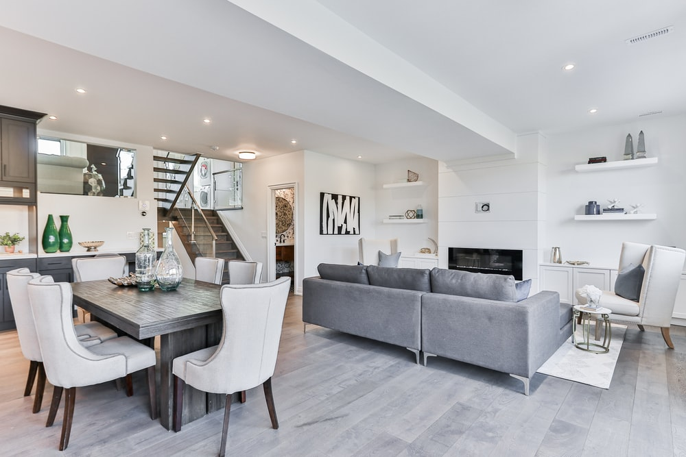 A Connecting Living Room and Kitchen with White Walls, Matching Dining Chairs, and Gray Custom Sofas, Among Other Things