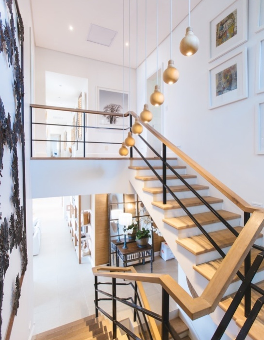 A Home Interior with White Walls, Wooden Stairs, Hanging Light Fixtures, and Wall Art
